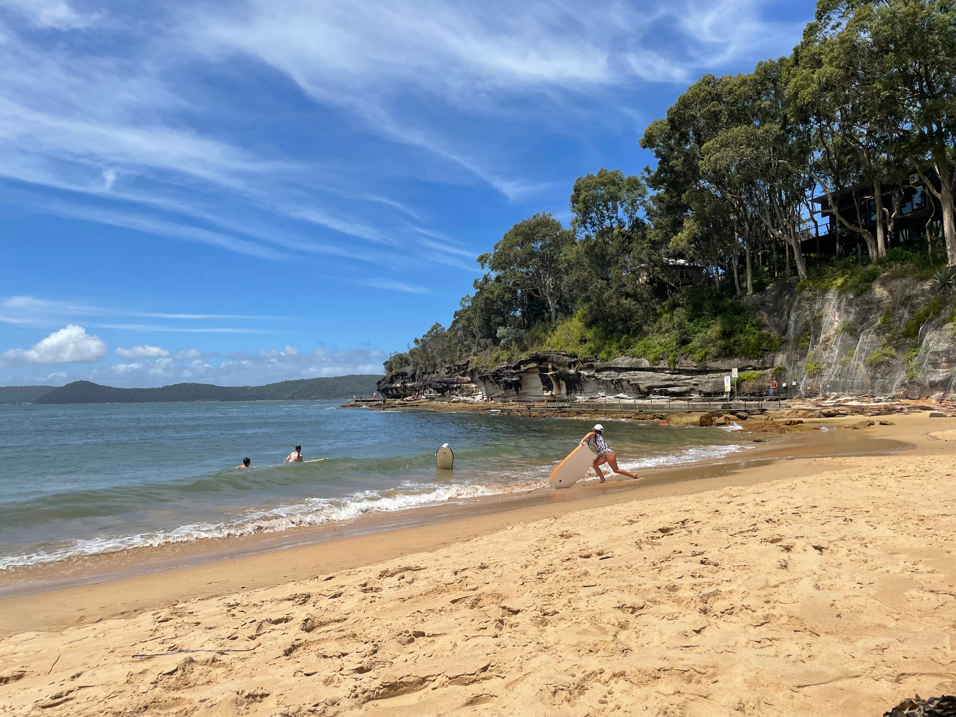 Pearl Beach cove with sandstone cliffs, calm water and a swimmer heading in with a bodyboard