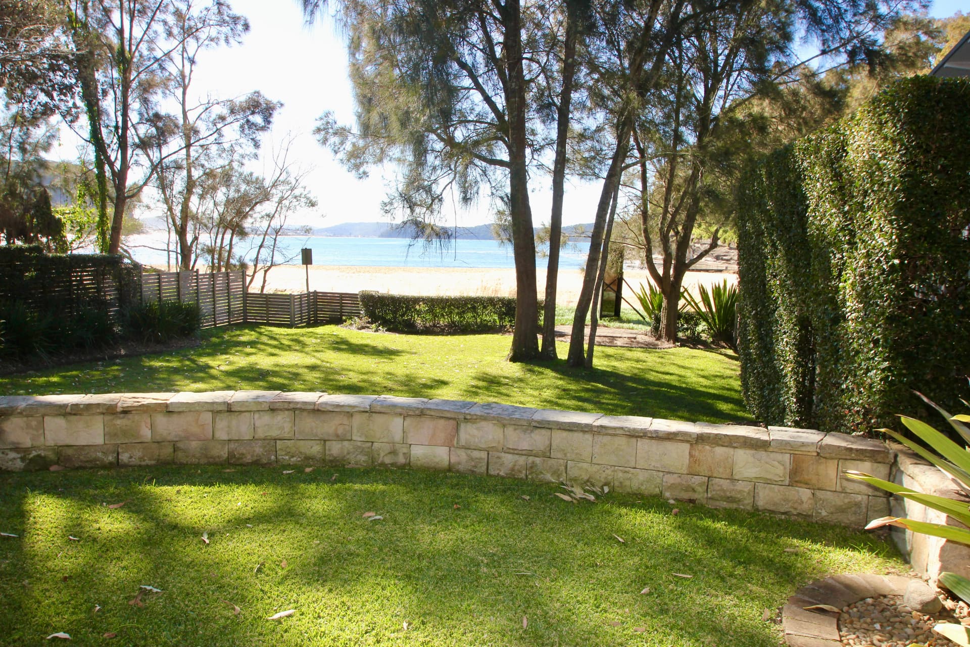 Back lawn and sandstone garden wall at The Gem looking through casuarinas to Pearl Beach and Broken Bay