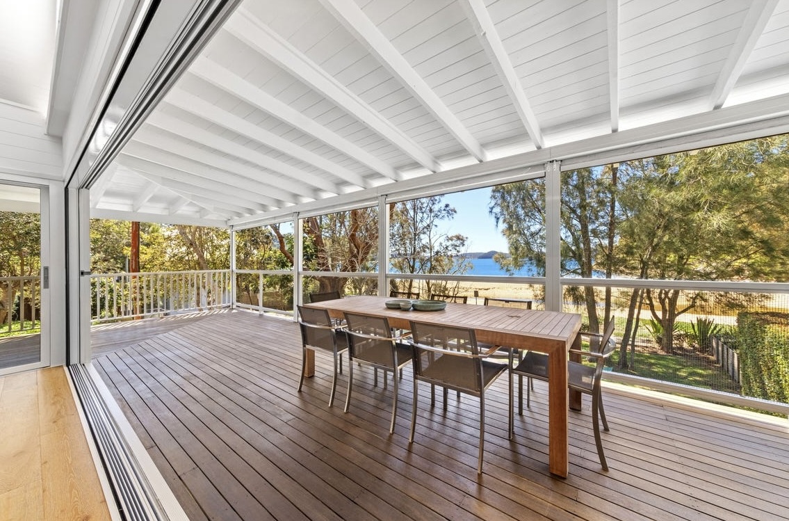 Covered upstairs deck with timber dining table and ocean views through the trees