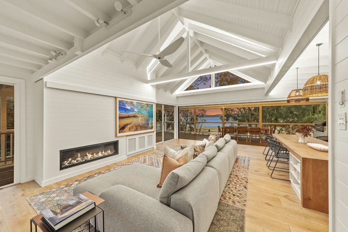 Upstairs living room at dusk — vaulted white ceilings and doors opening to the water