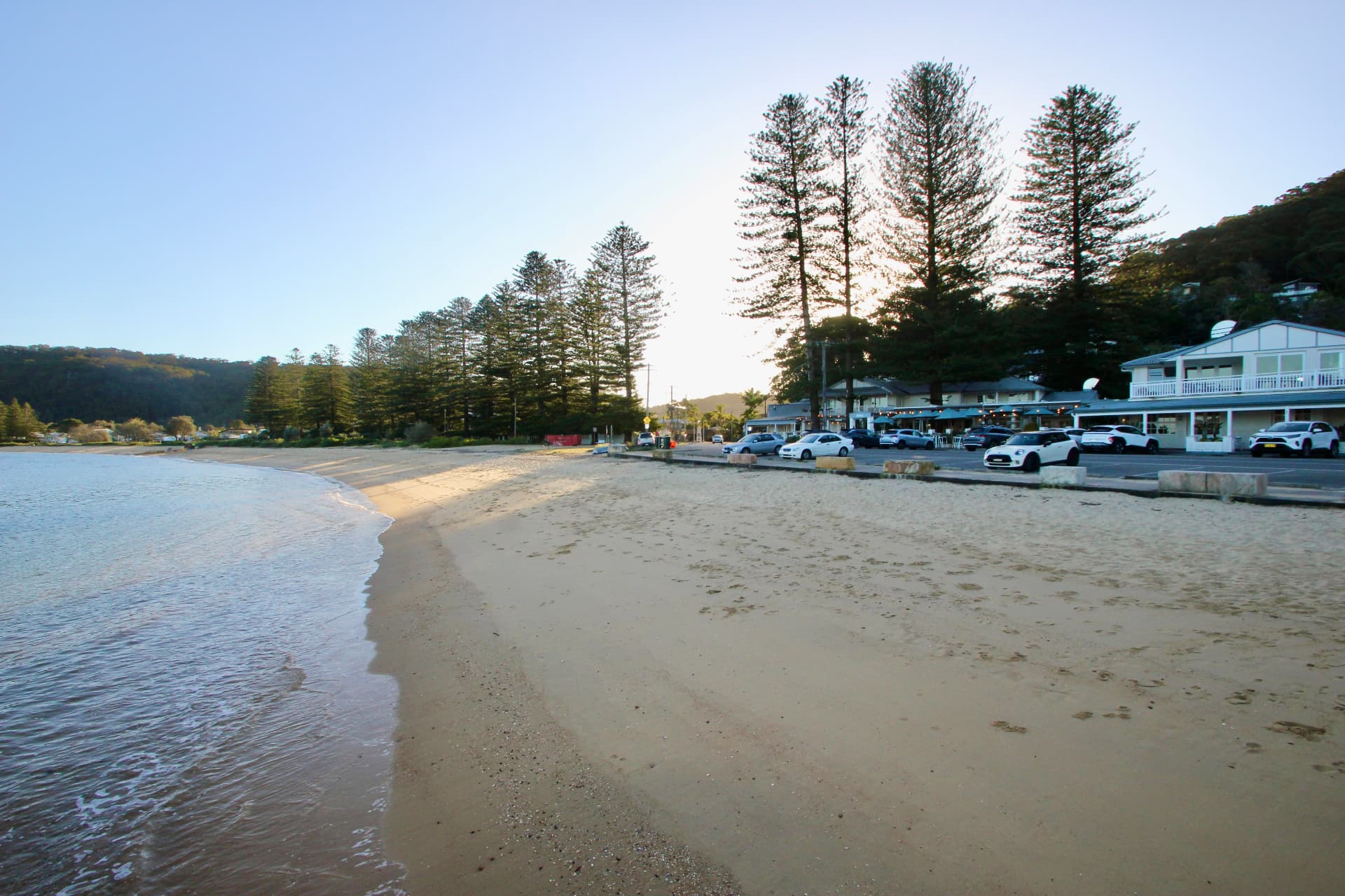 Patonga beach at golden hour — calm water, sand and Norfolk pines above the waterfront pub