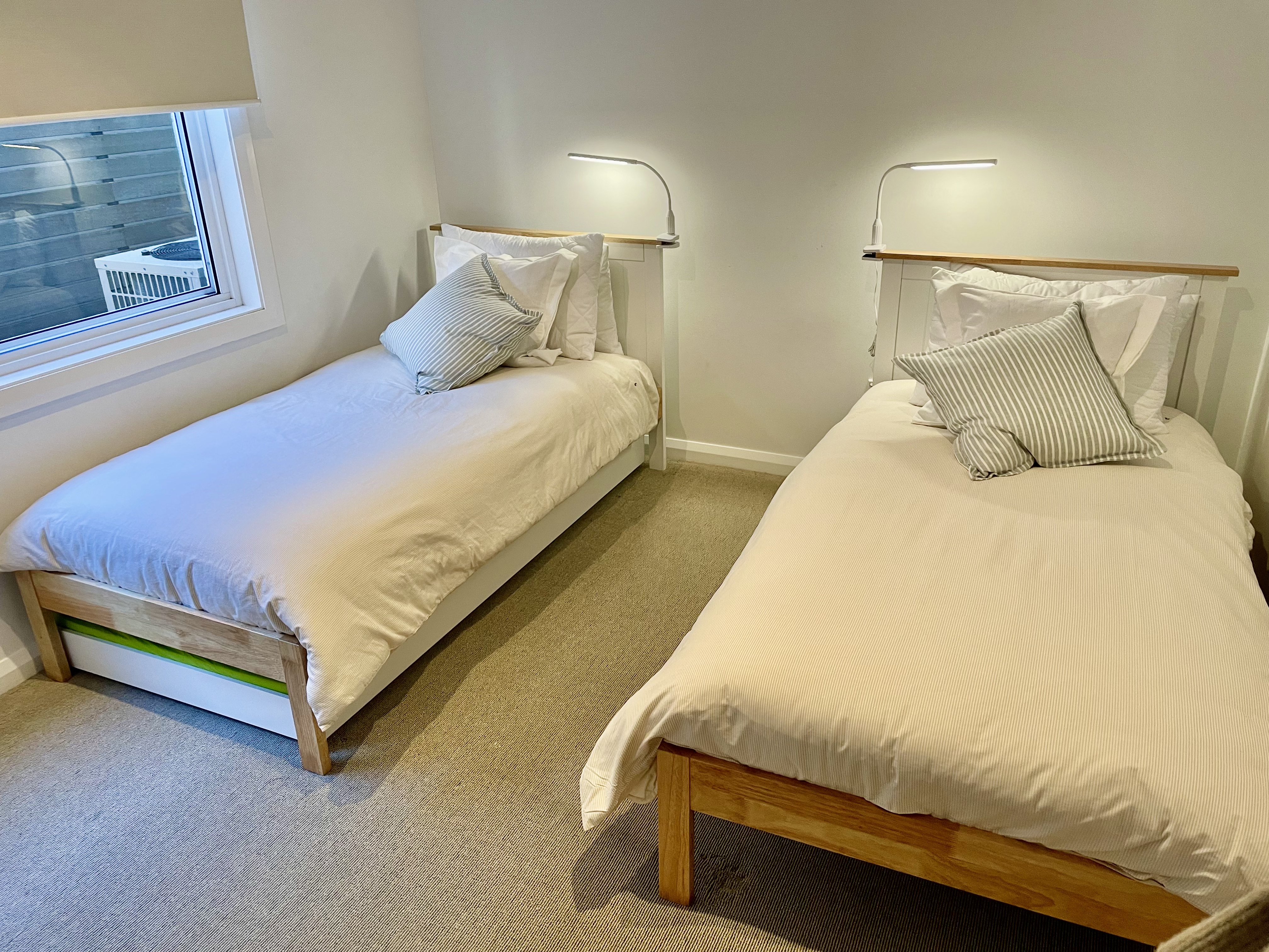 Downstairs second bedroom with two single beds, a pull-out trundle underneath and reading lamps above timber headboards