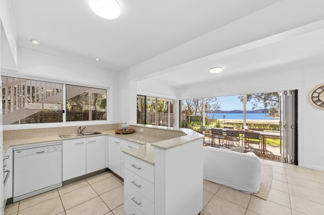Downstairs kitchen with white cabinetry looking through bifold doors to the deck and Pearl Beach beyond