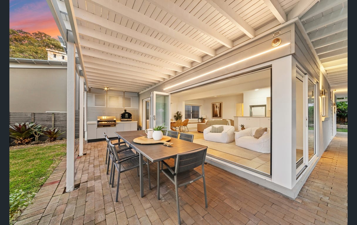 Downstairs covered terrace with outdoor dining table and BBQ, opening through wide doors to the living room