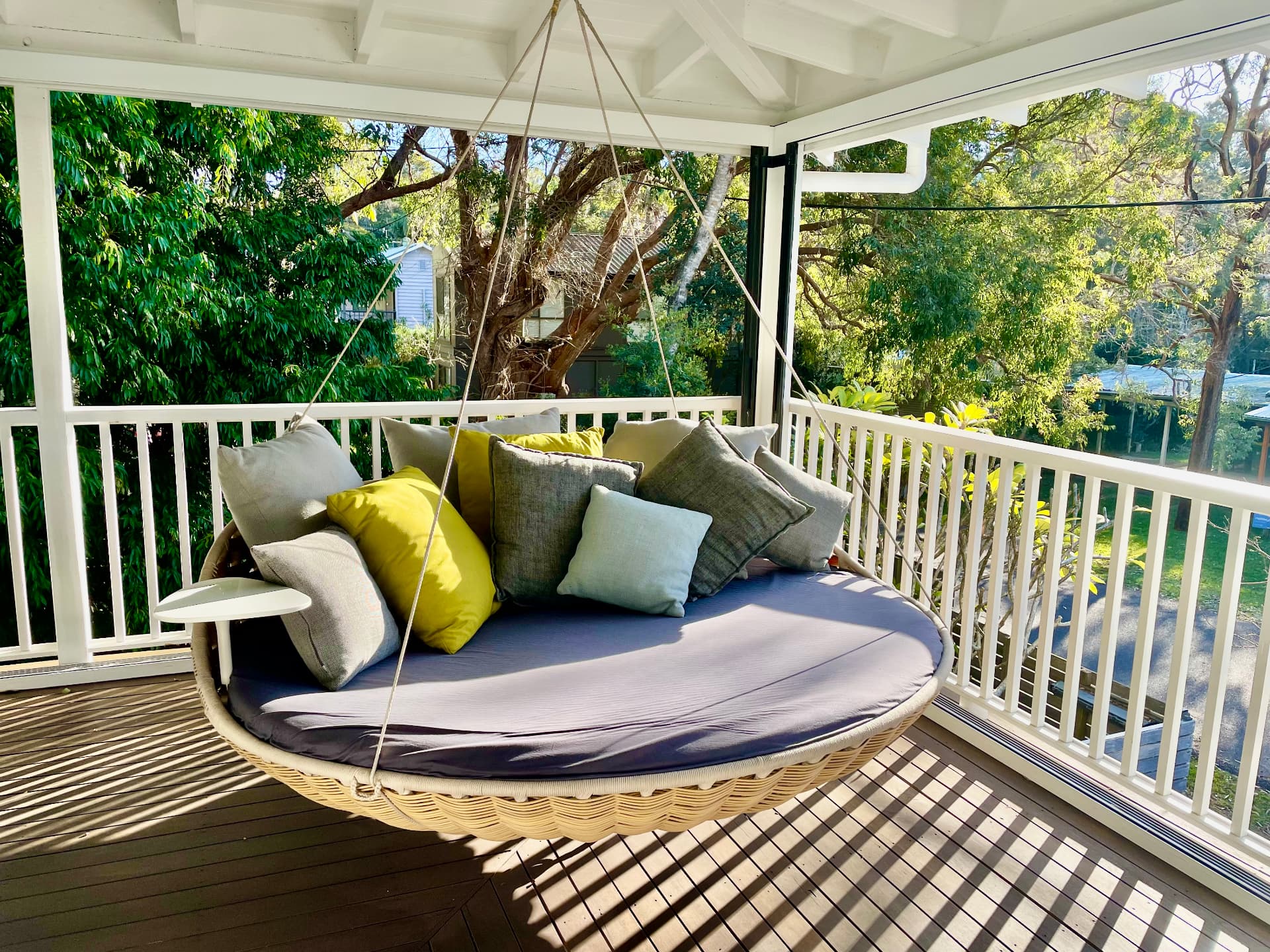 Round hanging swing daybed with cushions on the upstairs verandah, framed by gum trees