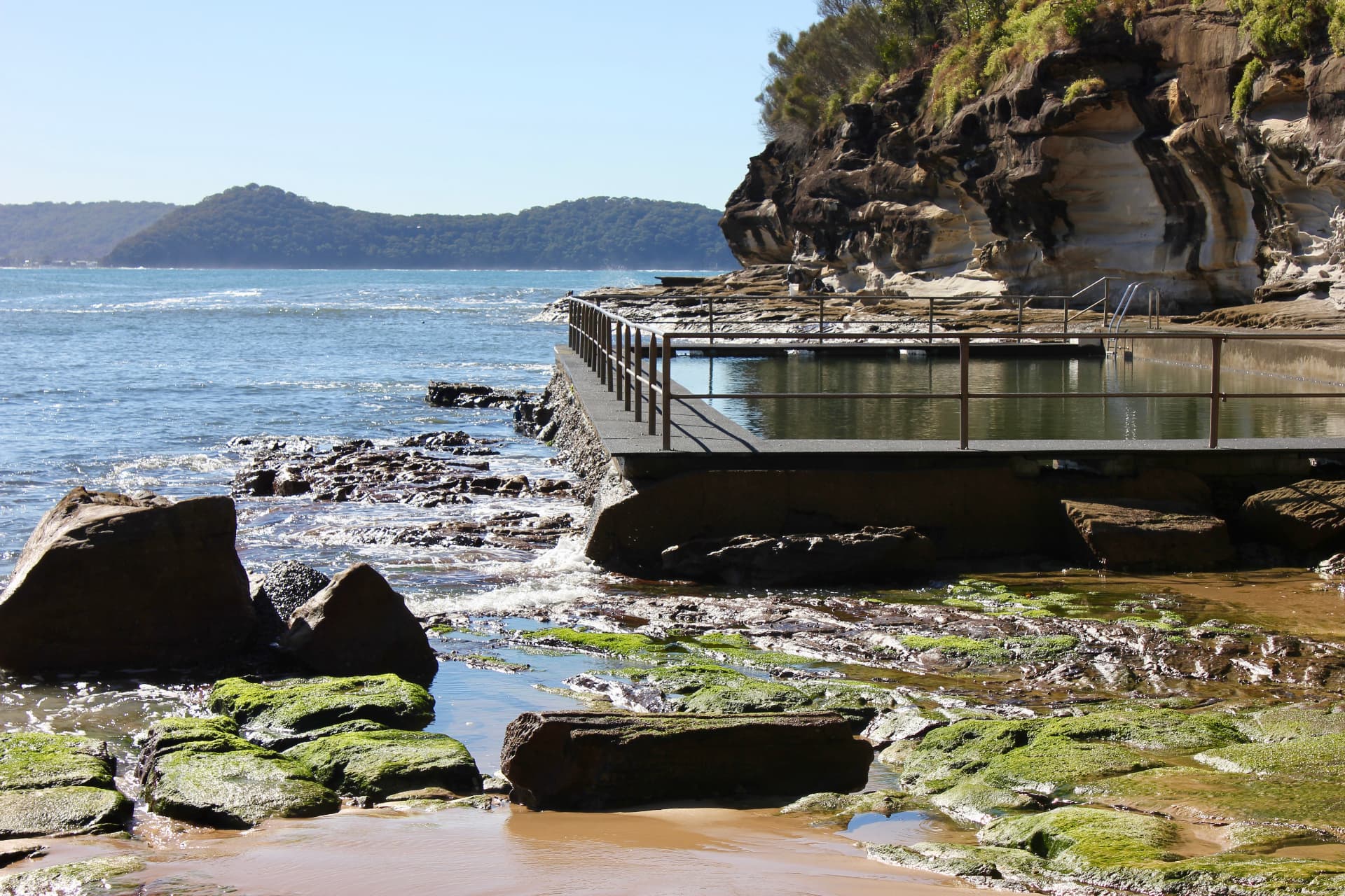 Pearl Beach ocean rock pool beside the sandstone cliffs with waves washing over the rock shelf