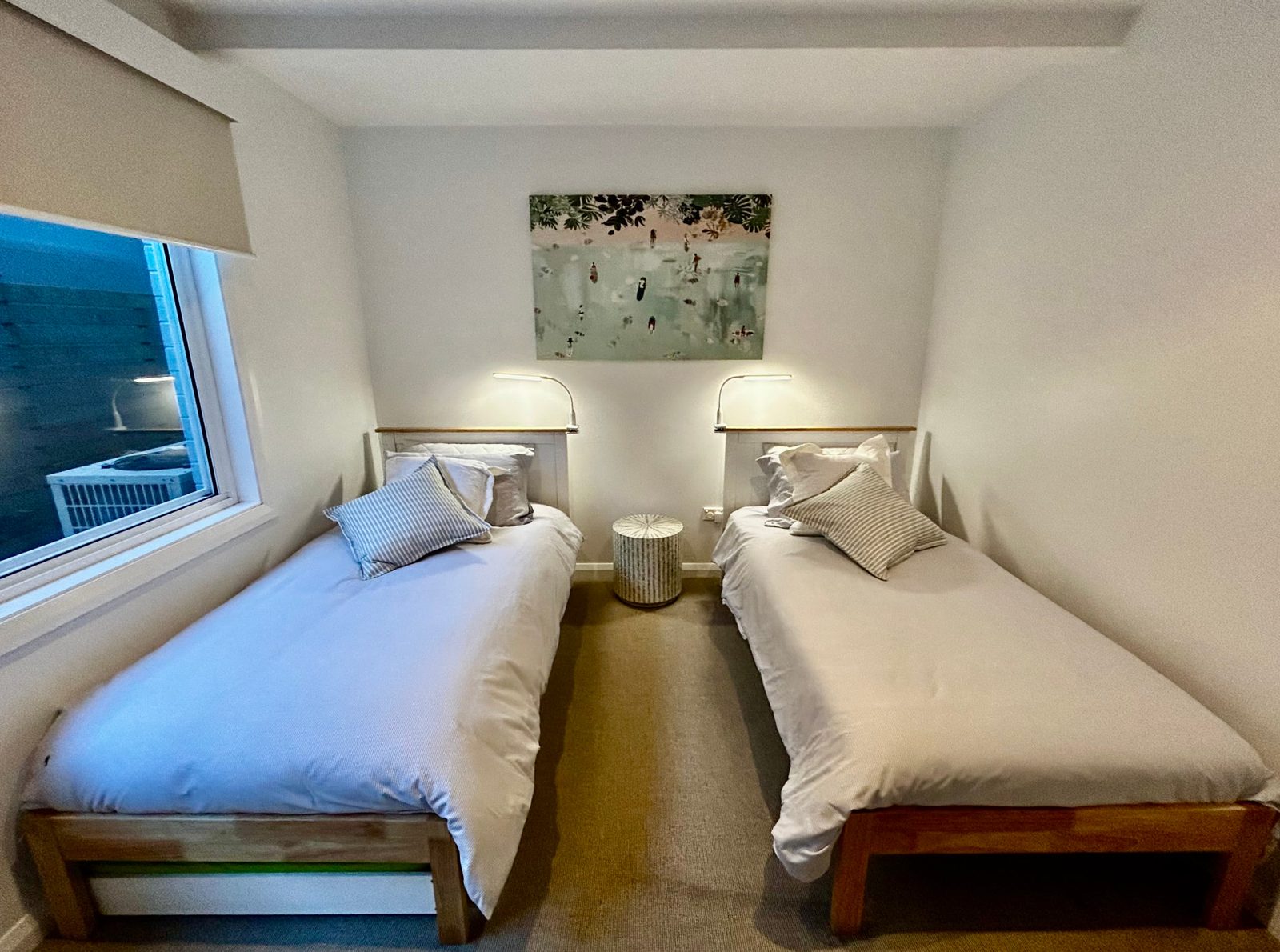 Downstairs second bedroom with two single beds, a pull-out trundle underneath and reading lamps above timber headboards