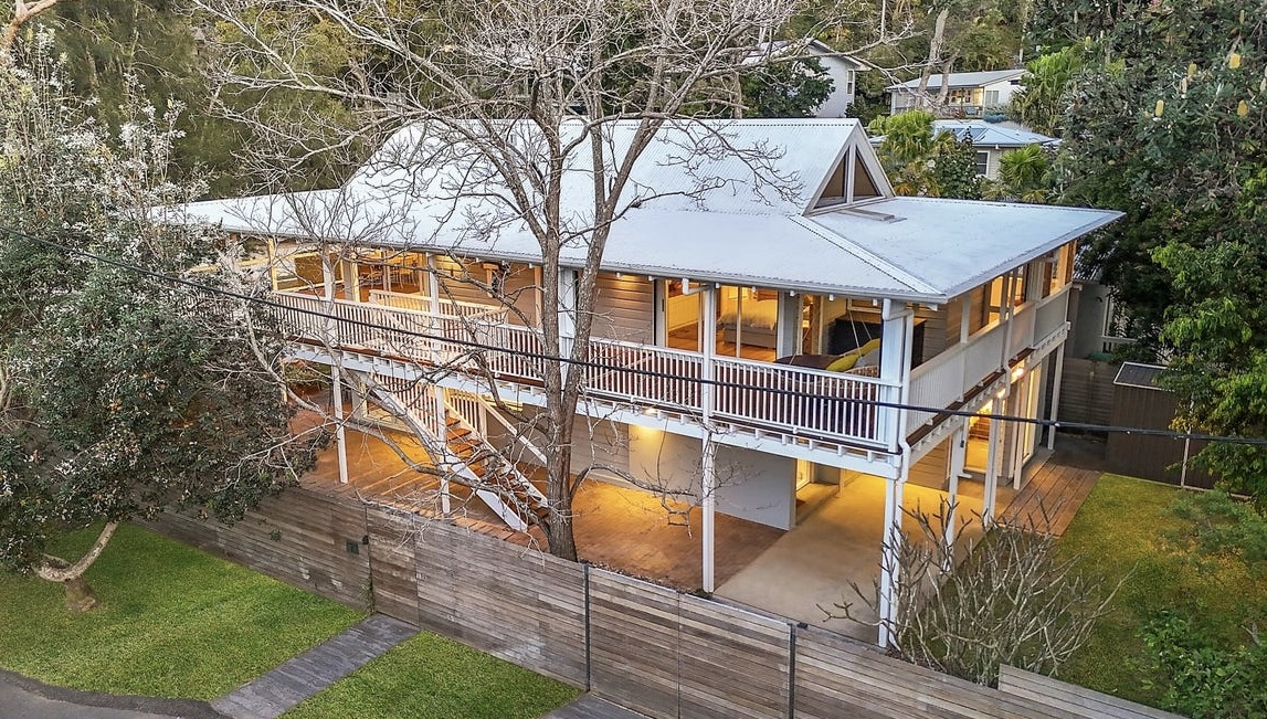 The Gem from the side at dusk — two-storey timber house with wraparound verandahs glowing warm through the trees