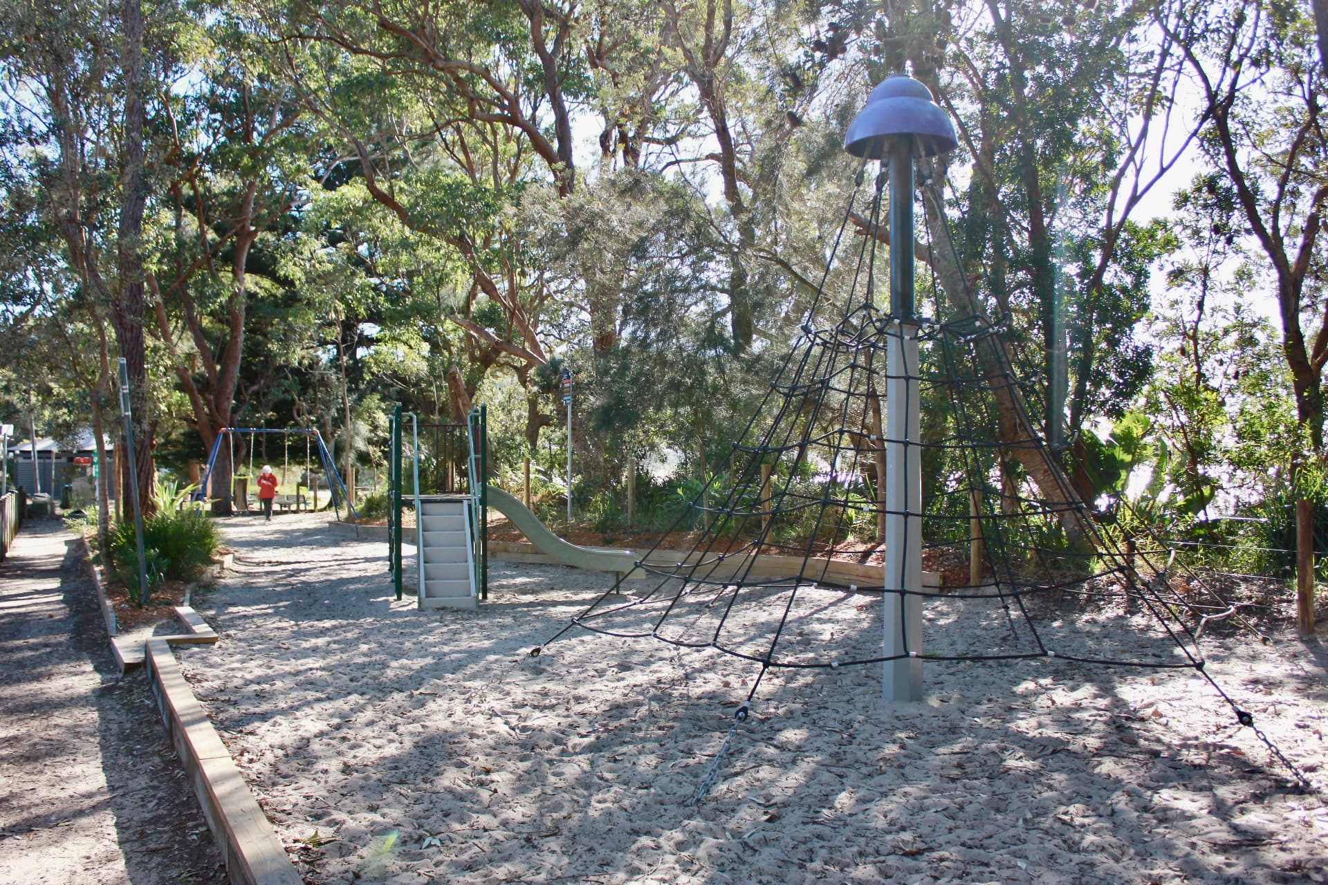 Shaded playground with climbing net, slide and swings under angophoras on the Pearl Beach foreshore