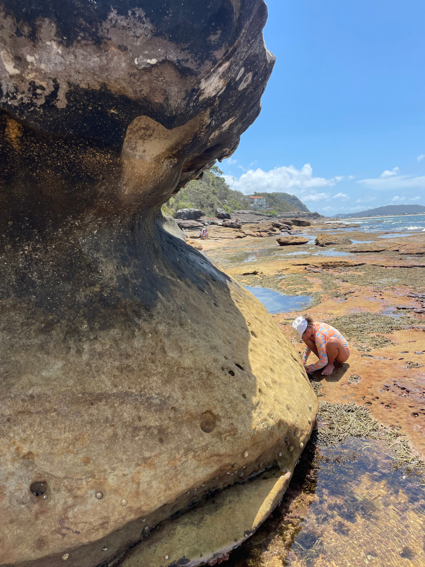 Child in a rashie exploring the sandstone rock shelf and tidal pools beside a huge weathered boulder