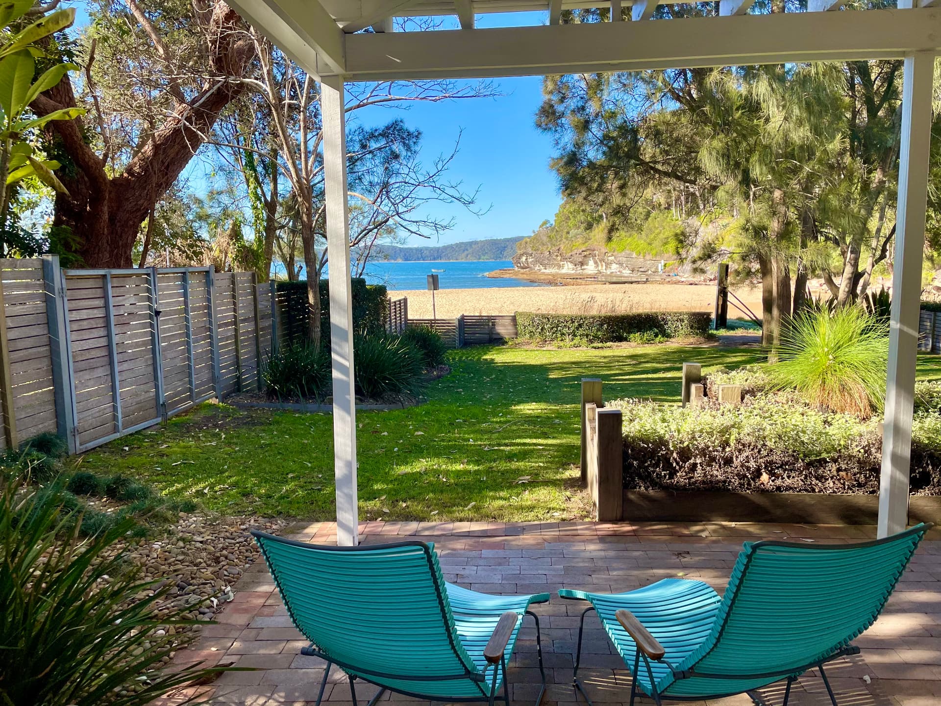 Two aqua lounge chairs under the pergola looking across the lawn and back gate to Pearl Beach