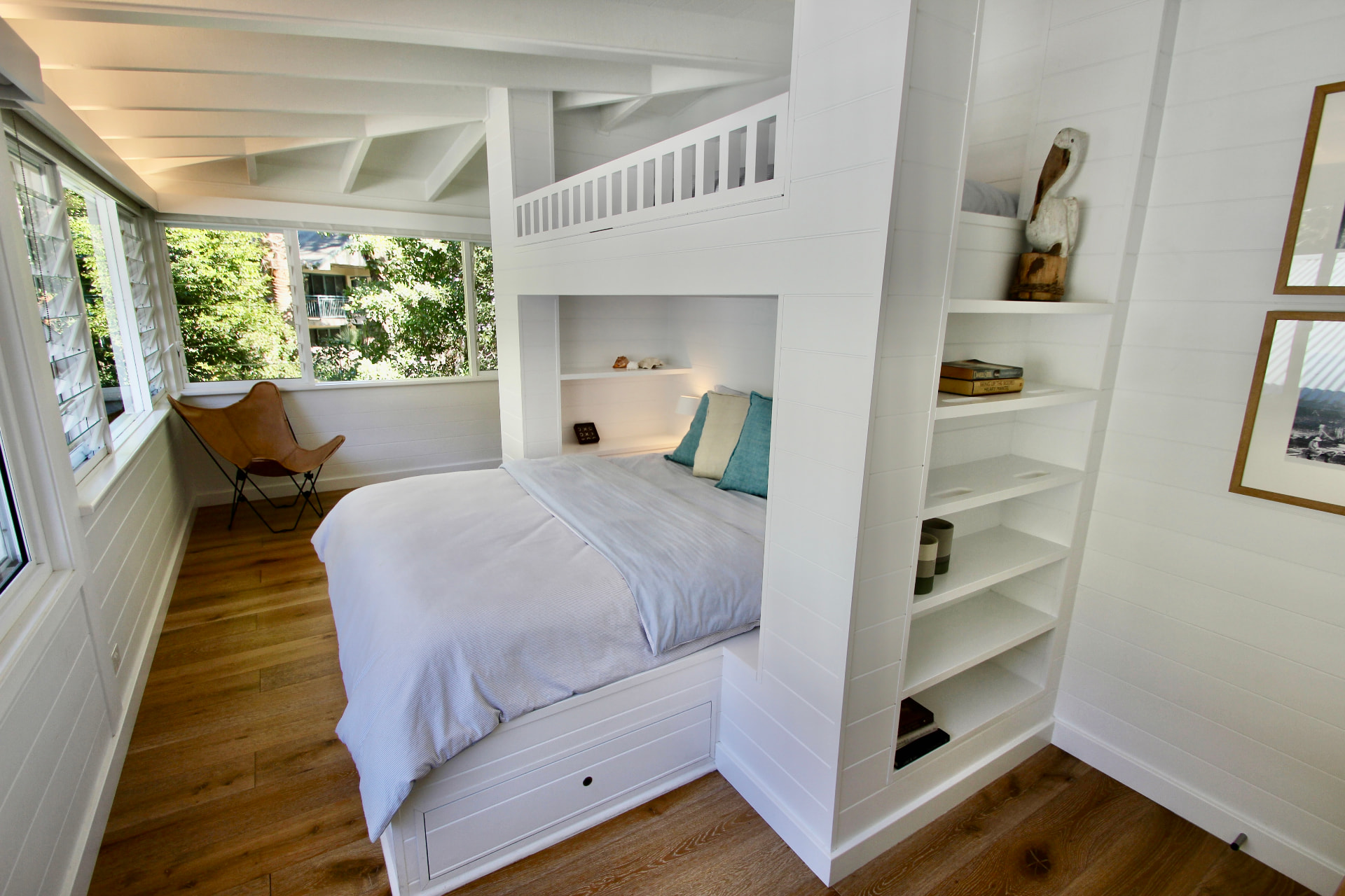 Upstairs second bedroom with a built-in queen bed, single bunk above and timber floors beside louvre windows