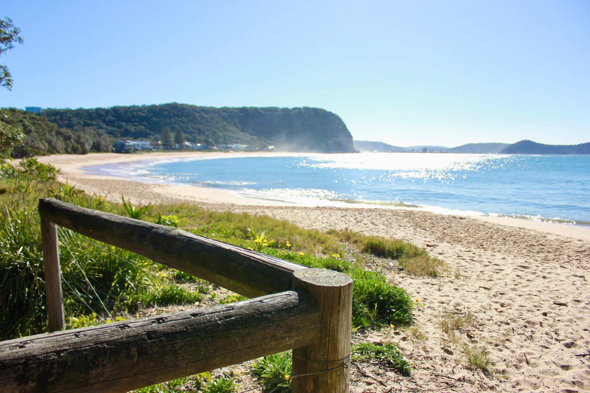 Timber fence at the beach entry looking along the crescent of Pearl Beach to the headland
