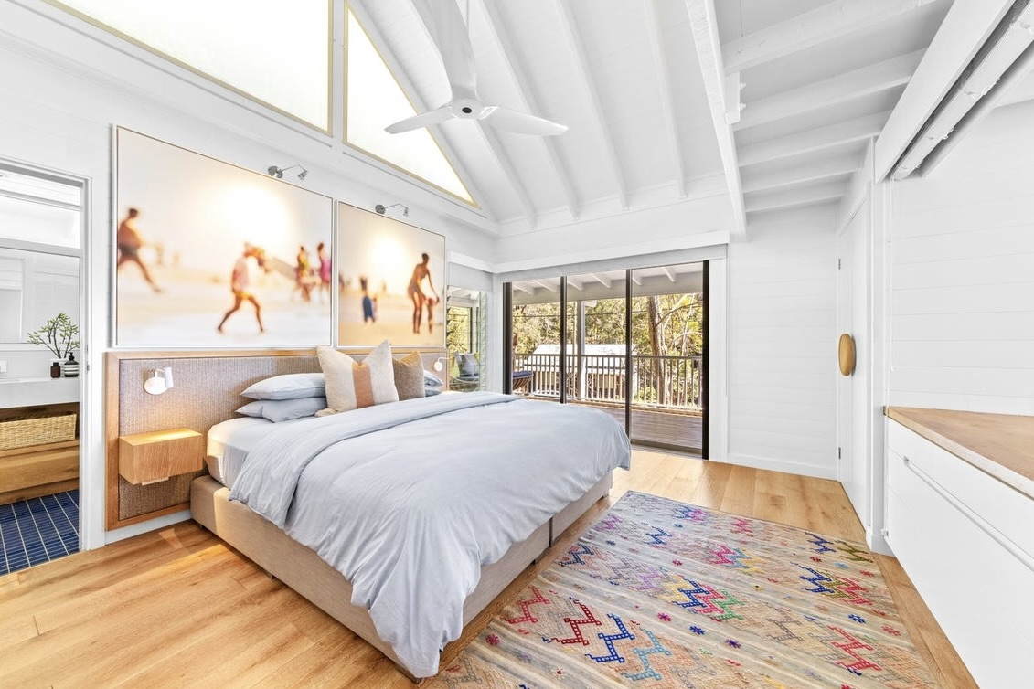 Upstairs master bedroom with vaulted ceiling, beach artwork and doors to the balcony