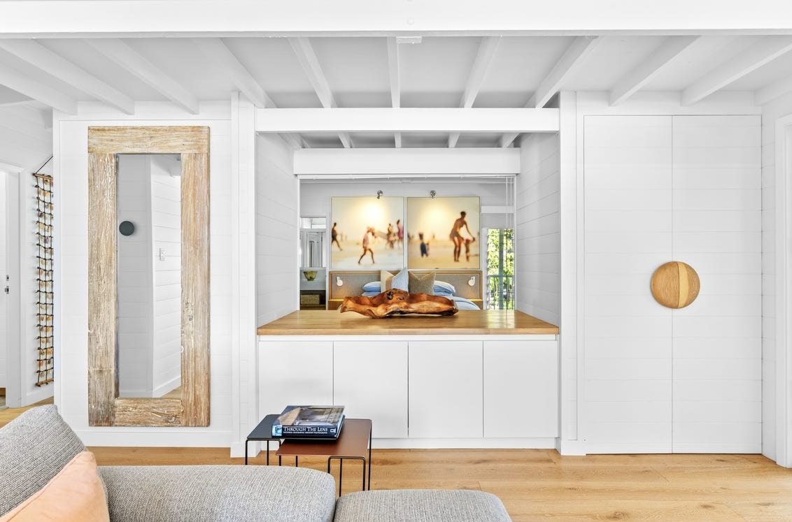 View from the upstairs living room through to the master bedroom, with a driftwood-framed mirror and beach artwork above the bed