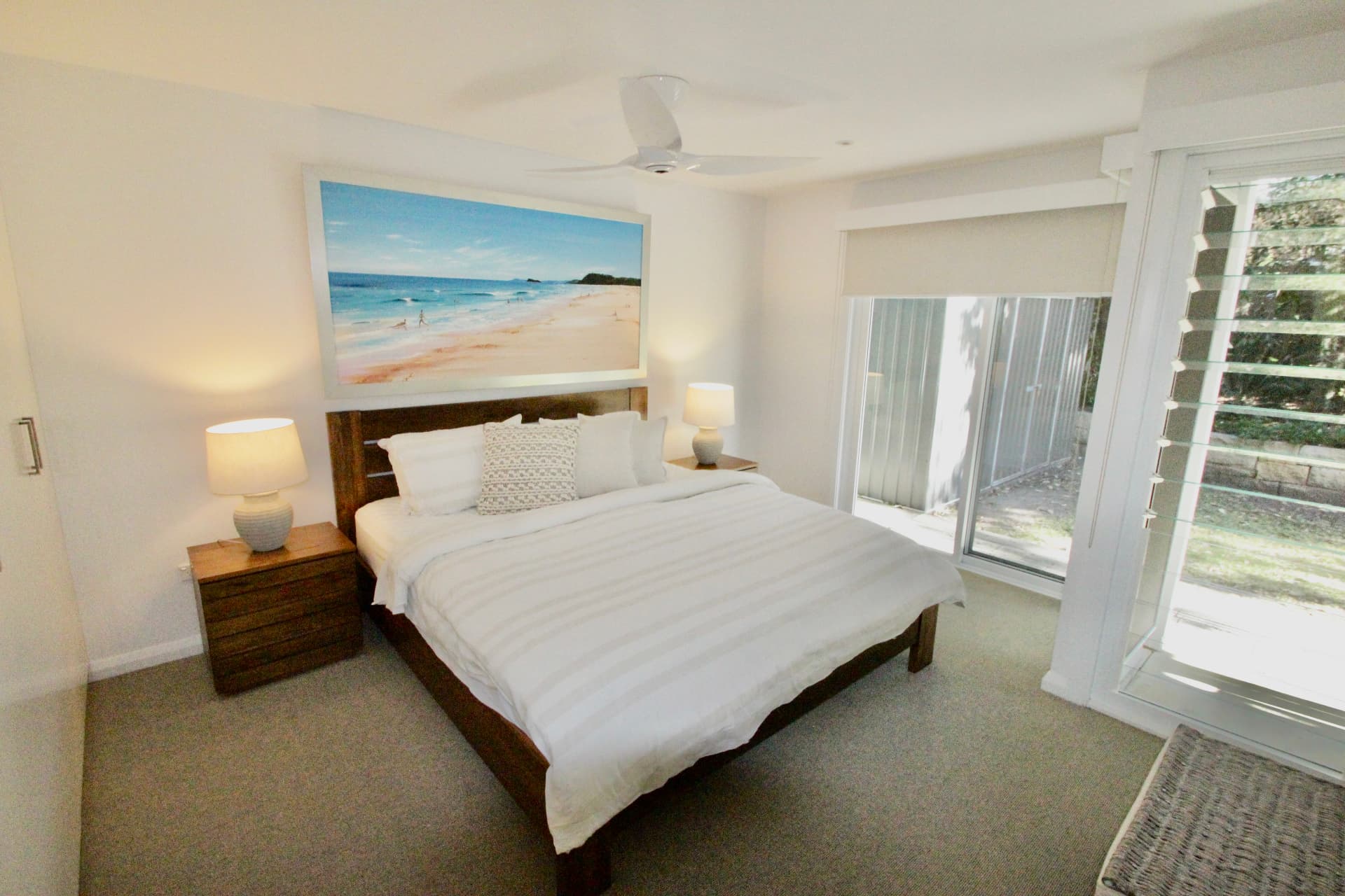 Downstairs master bedroom with king bed, timber side tables and louvre doors opening to the garden