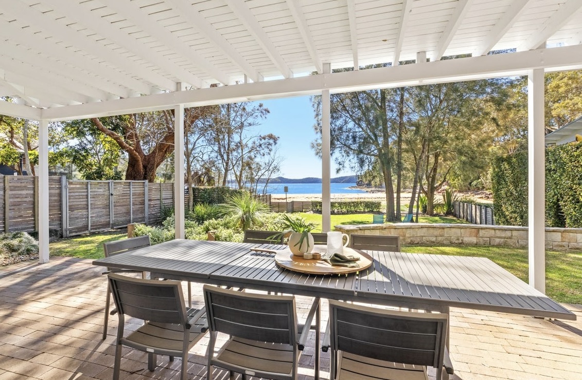 Covered outdoor dining terrace with table and chairs overlooking Pearl Beach