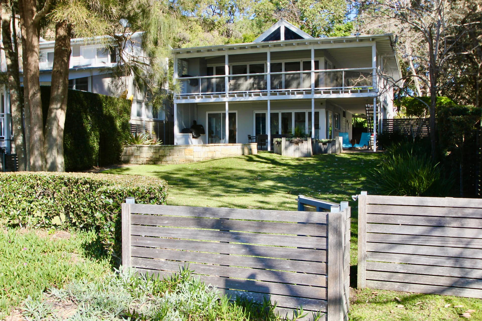 The Gem at 7 Gem Road, Pearl Beach seen from the beach side — timber gate, lawn and two-storey verandahs